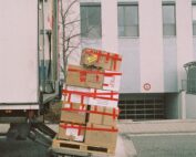 Brown boxes wrapped in red tape being loaded onto a large moving van.